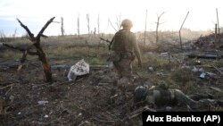 Украінскі вайсковец ідзе каля забітага расейскага салдата, ваколіцы Андрэеўкі ў Данецкай вобласьці, 16 верасьня 2023 году.