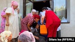 Медики скорой помощи пытаются помочь потерявшей сознание матери убитой девочки
