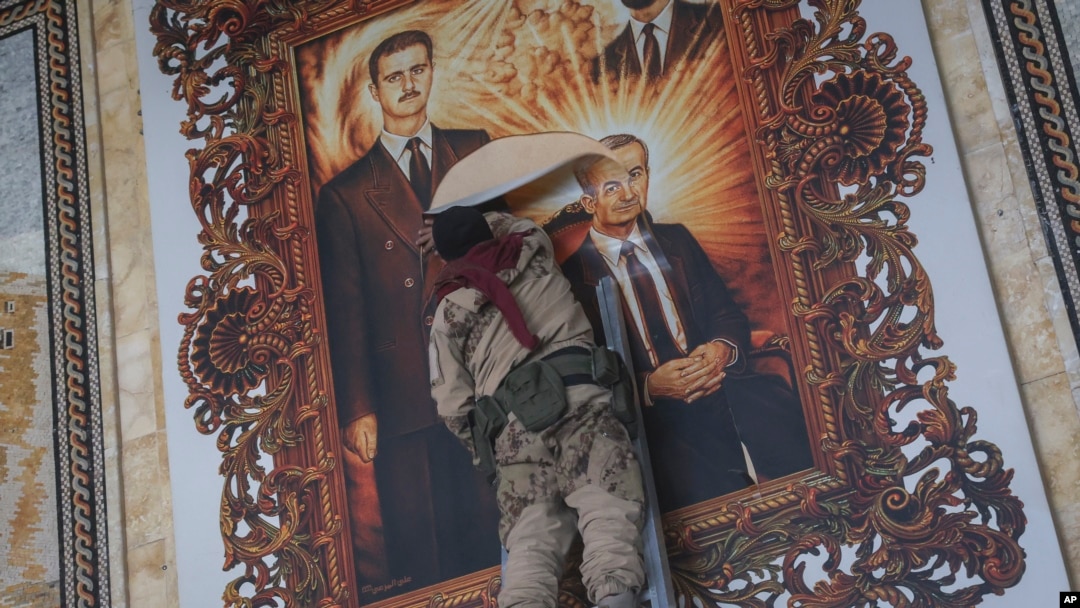 Боец "Хайят Тахрир аш-Шам" рвет картину, изображающую президента Сирии Башара Асада и его покойного отца Хафеза Асада. Международный аэропорт Алеппо, 2 декабря 2024 года
