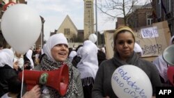 Belgiýanyň Genk şäherinde ak hijap daňnan musulman zenanlary özleriniň baş örtgüleri sebäpli "HEMA" dükanlar toplumyndan işden çykarylmaklaryna protest bildirýärler. Genk, mart, 2011.