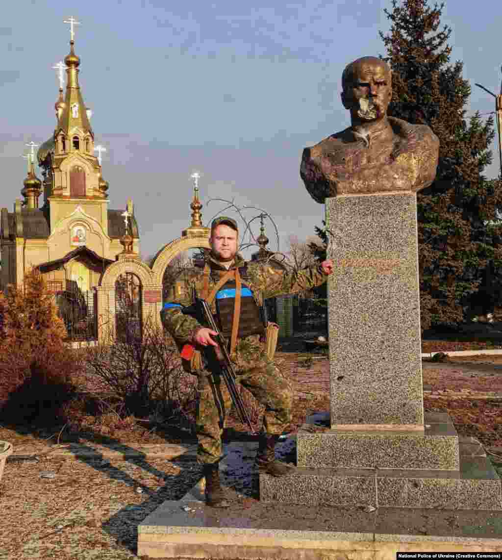 Український військовий позує біля тоді ще цілого пам'ятника Шевченку в Мар'їнці в березні 2022 року