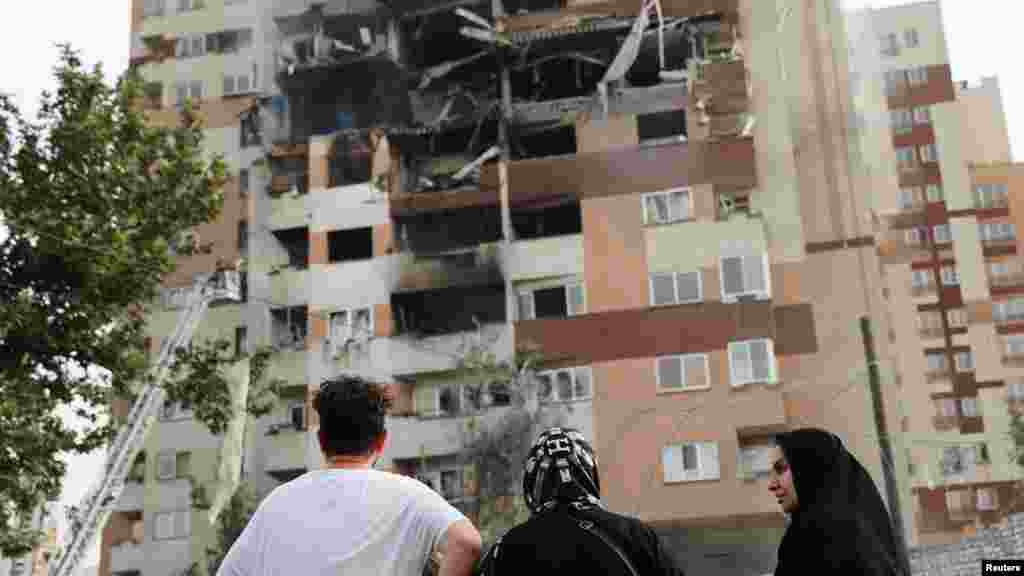 Oamenii se uită la o clădire avariată în urma loviturilor israeliene din Teheran, pe 13 iunie.